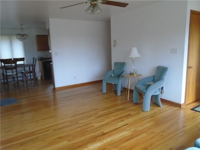 sitting room featuring baseboards, wood finished floors, and ceiling fan with notable chandelier