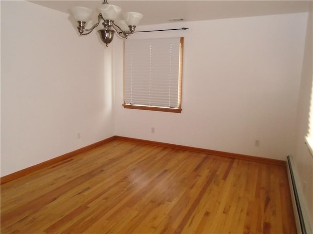 unfurnished room featuring a baseboard radiator, an inviting chandelier, light wood finished floors, and baseboards