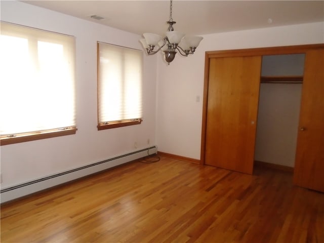 unfurnished bedroom featuring multiple windows, an inviting chandelier, hardwood / wood-style floors, and a baseboard heating unit