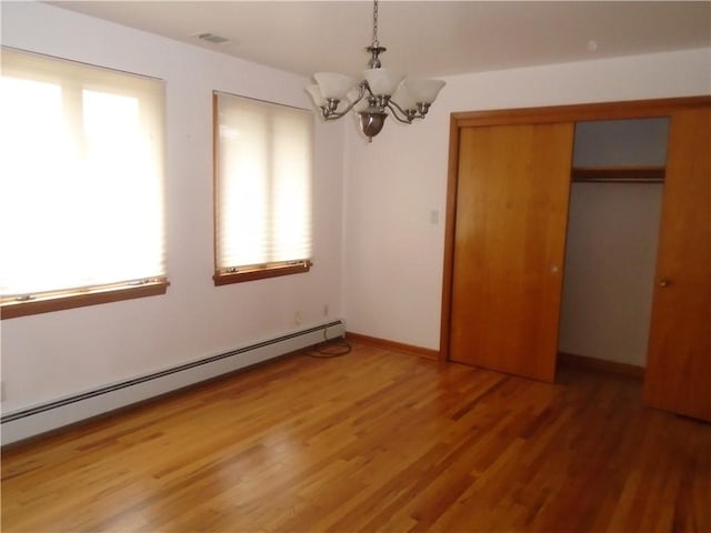 unfurnished bedroom featuring visible vents, a baseboard heating unit, light wood-type flooring, a closet, and a notable chandelier