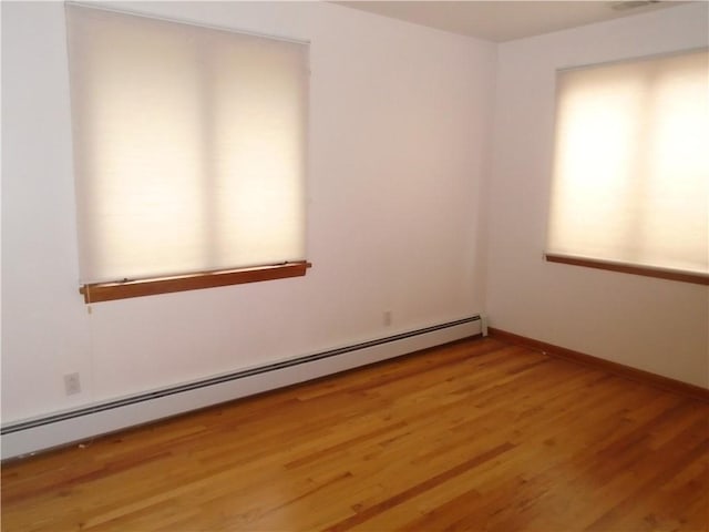 unfurnished room with baseboard heating, baseboards, and light wood-style flooring