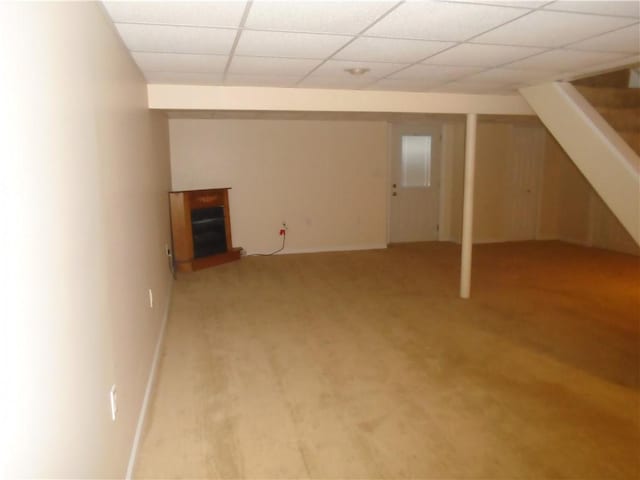 finished below grade area with stairway, a fireplace with raised hearth, light carpet, baseboards, and a paneled ceiling
