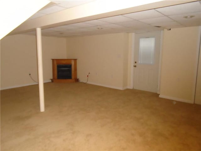 finished basement with a paneled ceiling, a fireplace with raised hearth, baseboards, and light carpet