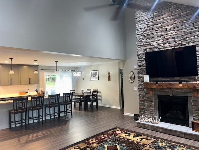 living room featuring ceiling fan, a stone fireplace, dark hardwood / wood-style floors, and vaulted ceiling