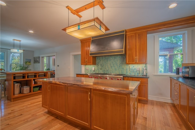 kitchen featuring light wood-type flooring, a healthy amount of sunlight, a kitchen island, custom range hood, and hanging light fixtures