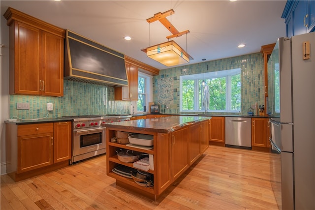 kitchen with light wood-type flooring, custom range hood, decorative light fixtures, stainless steel appliances, and backsplash