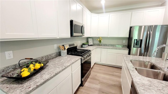 kitchen with appliances with stainless steel finishes, a sink, light wood finished floors, white cabinets, and light stone counters