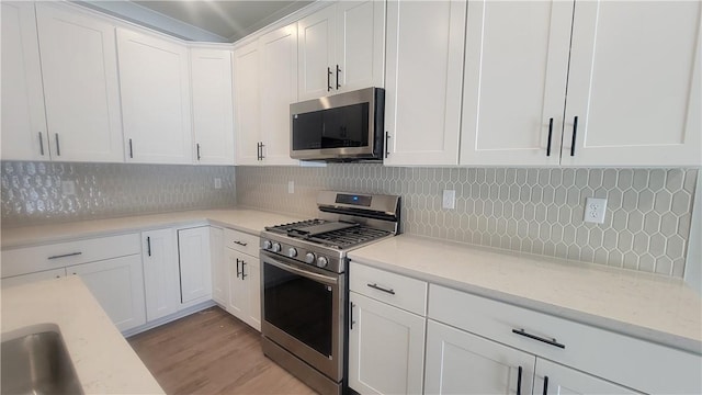 kitchen with stainless steel appliances, white cabinetry, decorative backsplash, light wood-type flooring, and light stone counters