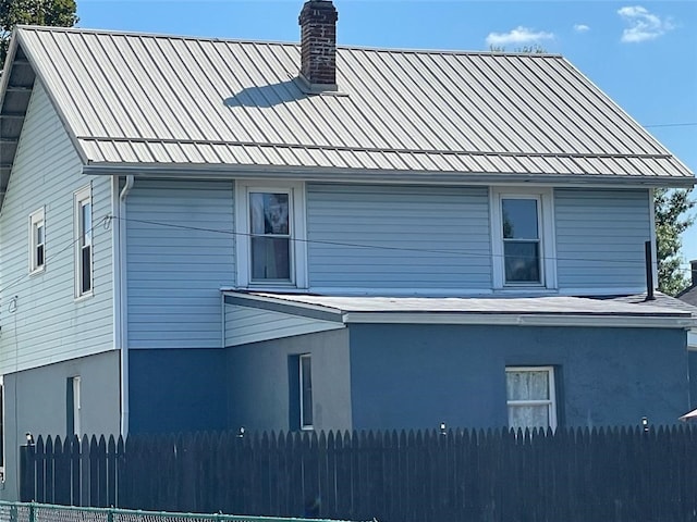 view of side of property with a chimney, fence, stucco siding, and metal roof