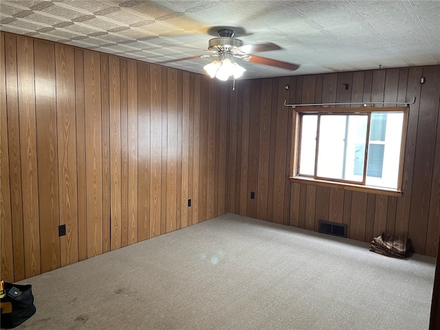 carpeted spare room with wood walls and ceiling fan