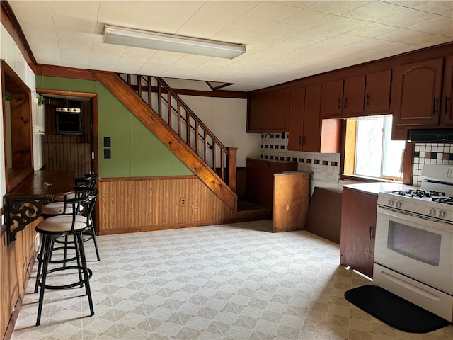 kitchen with wood walls, a kitchen bar, and white range with gas cooktop