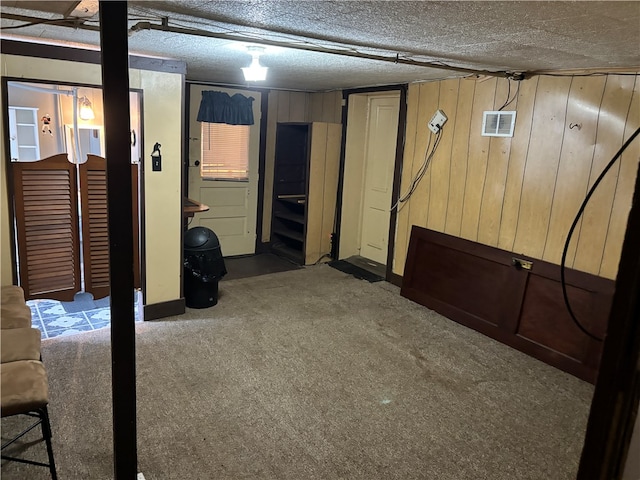 basement with a textured ceiling, carpet, and wood walls