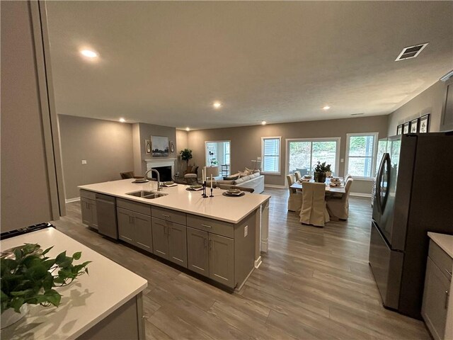 kitchen with sink, a center island with sink, hardwood / wood-style floors, gray cabinets, and stainless steel appliances