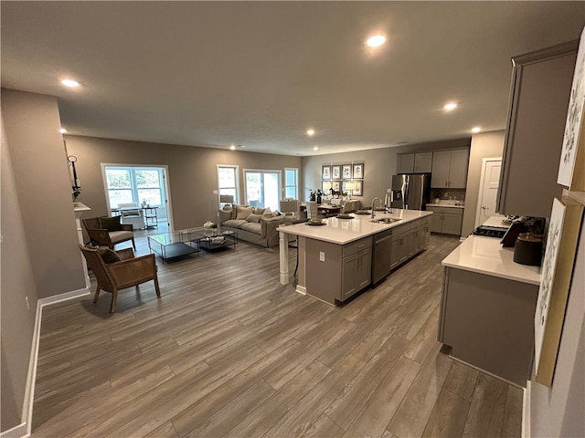 kitchen featuring stainless steel appliances, a kitchen breakfast bar, hardwood / wood-style floors, an island with sink, and gray cabinets