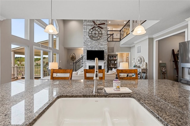 kitchen featuring stone countertops, a towering ceiling, a fireplace, hanging light fixtures, and ornamental molding