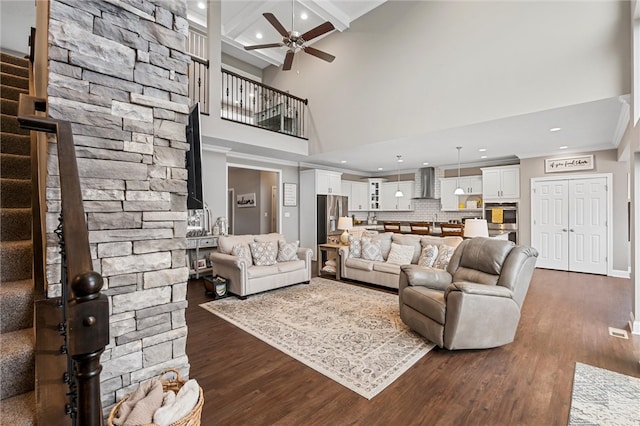 living room featuring ceiling fan, beamed ceiling, dark wood-type flooring, and a high ceiling