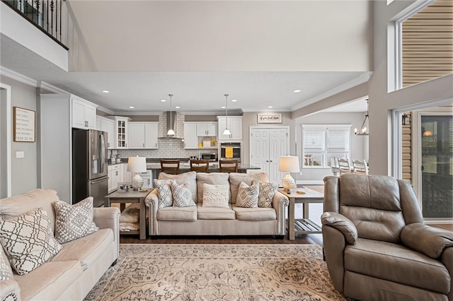 living room featuring light hardwood / wood-style floors, crown molding, a high ceiling, and a notable chandelier