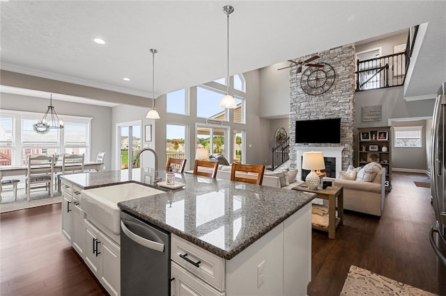 kitchen with a stone fireplace, white cabinets, dark hardwood / wood-style flooring, a center island with sink, and dishwasher