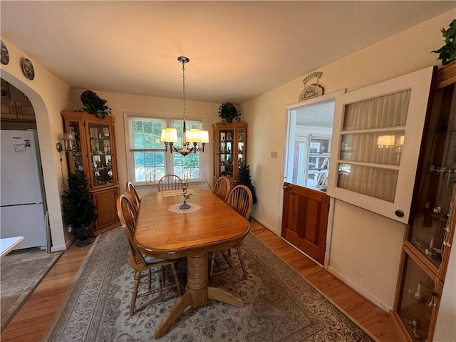 dining room with arched walkways, a chandelier, and wood finished floors