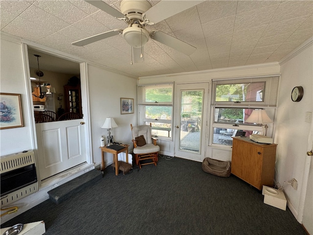 living area featuring heating unit, crown molding, dark carpet, and ceiling fan