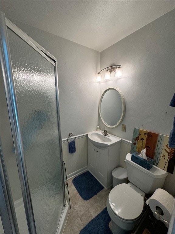 bathroom featuring a textured ceiling, vanity, toilet, and a shower with door