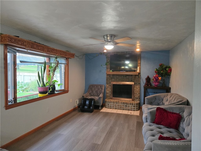 living room with a brick fireplace, ceiling fan, and wood-type flooring