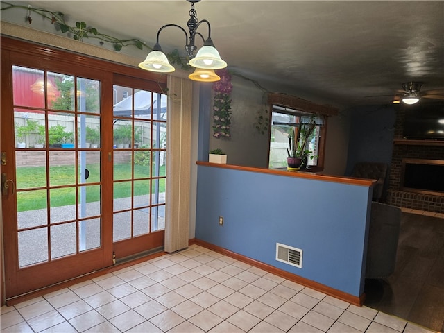 unfurnished dining area featuring ceiling fan with notable chandelier, a brick fireplace, and plenty of natural light