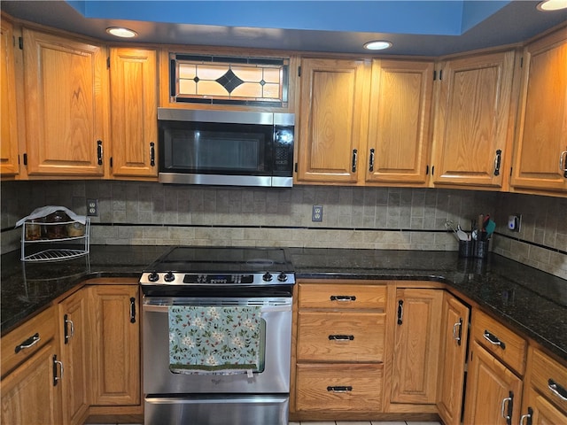 kitchen featuring decorative backsplash, appliances with stainless steel finishes, and dark stone counters