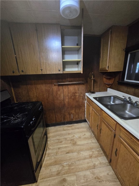 kitchen featuring light hardwood / wood-style floors, wooden walls, black gas range oven, and sink