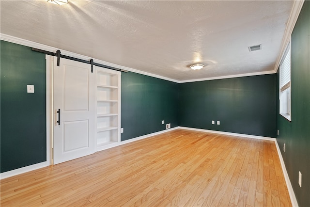 unfurnished bedroom featuring a barn door, a textured ceiling, ornamental molding, and hardwood / wood-style floors