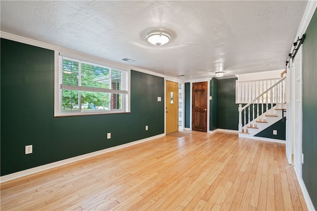 interior space with light hardwood / wood-style flooring, a textured ceiling, crown molding, and a barn door