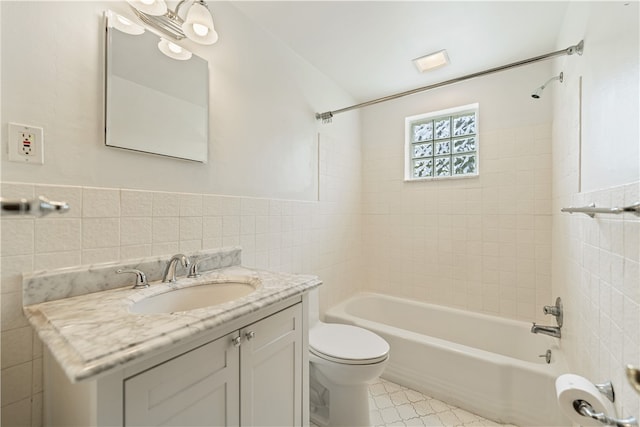 full bathroom with tile walls, tiled shower / bath combo, vanity, and toilet