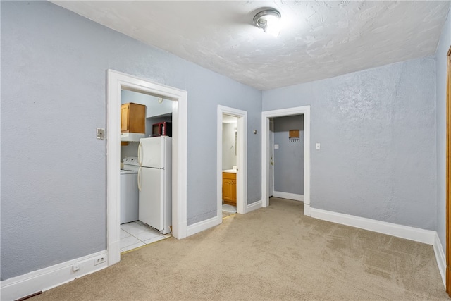 unfurnished bedroom featuring light carpet, washer / clothes dryer, white refrigerator, and connected bathroom