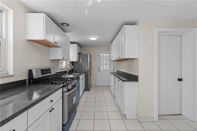 kitchen featuring dark stone countertops, gas range, sink, white cabinets, and light tile patterned floors