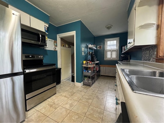 kitchen featuring radiator, sink, a textured ceiling, white cabinets, and appliances with stainless steel finishes