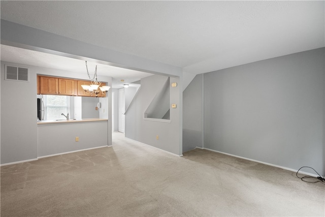 unfurnished living room with light carpet, an inviting chandelier, and sink