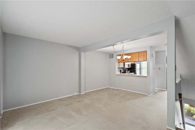 unfurnished living room featuring light carpet, a chandelier, and a healthy amount of sunlight