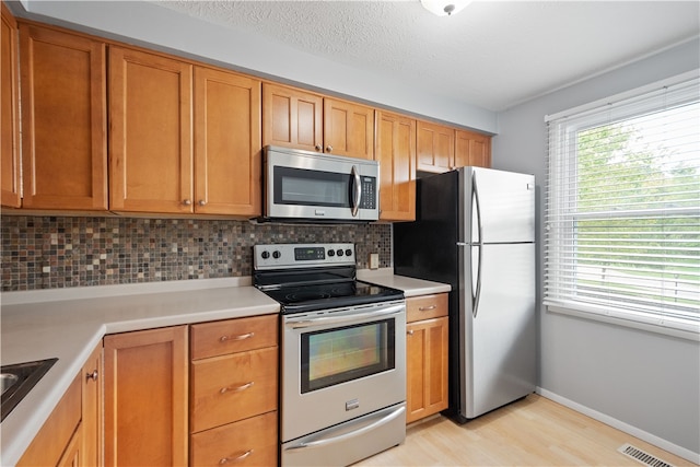 kitchen featuring a textured ceiling, appliances with stainless steel finishes, light hardwood / wood-style floors, and decorative backsplash