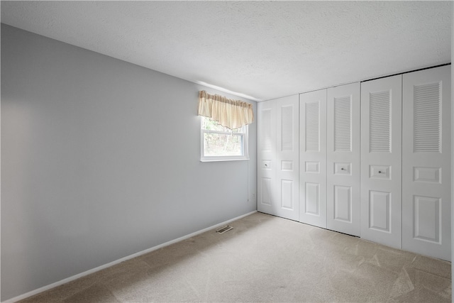 unfurnished bedroom with a textured ceiling, light colored carpet, and a closet