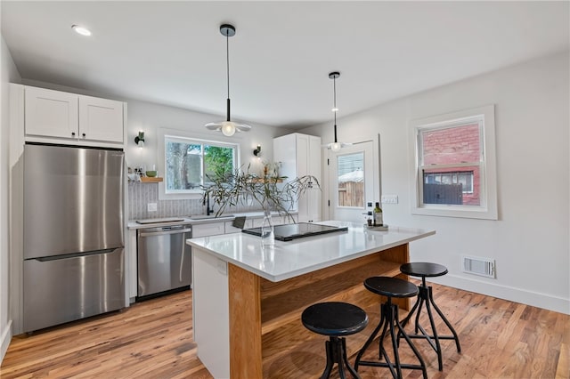 kitchen featuring tasteful backsplash, appliances with stainless steel finishes, light wood-type flooring, pendant lighting, and white cabinets