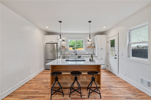 kitchen featuring light wood-type flooring, a center island, white cabinets, stainless steel refrigerator, and a breakfast bar