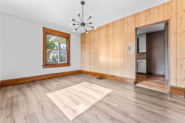 spare room featuring wood-type flooring, an inviting chandelier, and wood walls