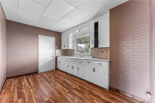 kitchen featuring white cabinets, wood walls, dark wood-type flooring, and a paneled ceiling