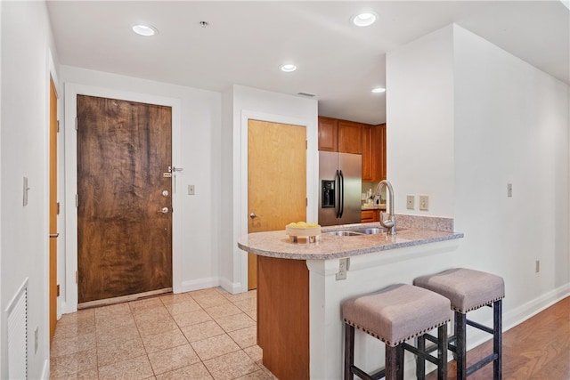 kitchen with sink, kitchen peninsula, light hardwood / wood-style flooring, stainless steel refrigerator with ice dispenser, and a kitchen bar