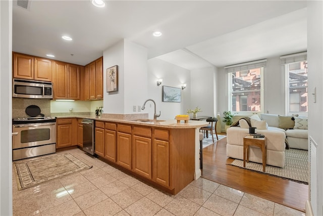 kitchen with light wood-type flooring, sink, kitchen peninsula, decorative backsplash, and appliances with stainless steel finishes