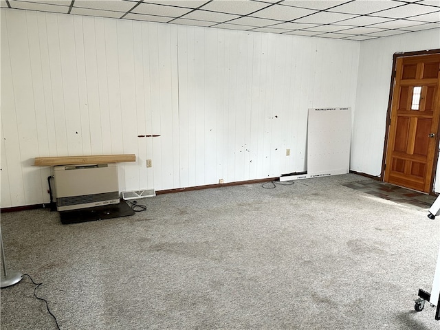 interior space with a drop ceiling, wood walls, and carpet flooring