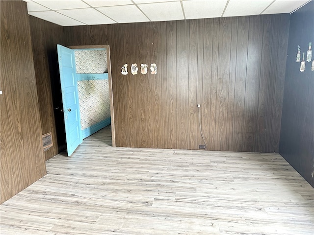 unfurnished room with a drop ceiling, wooden walls, and light hardwood / wood-style floors