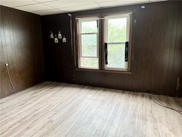 empty room featuring wooden walls, a drop ceiling, and light hardwood / wood-style floors