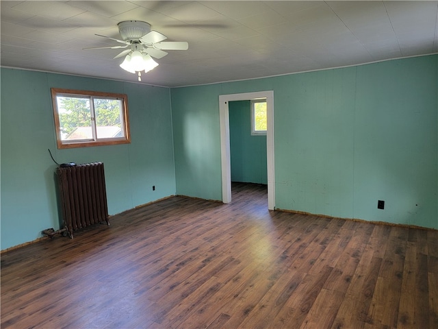 spare room featuring a healthy amount of sunlight, ceiling fan, radiator heating unit, and dark hardwood / wood-style flooring