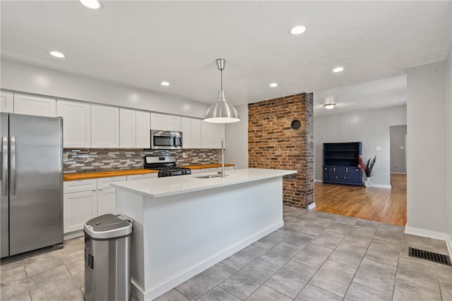 kitchen with decorative light fixtures, a kitchen island with sink, stainless steel appliances, and white cabinets